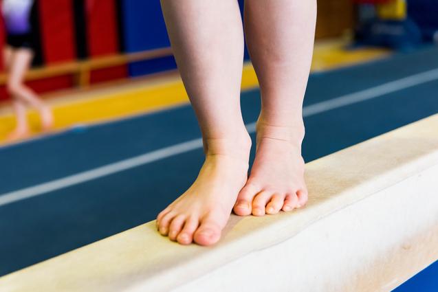 Füße eines Kindes stehen auf einem schmalen Turnbalken in einer Sporthalle.